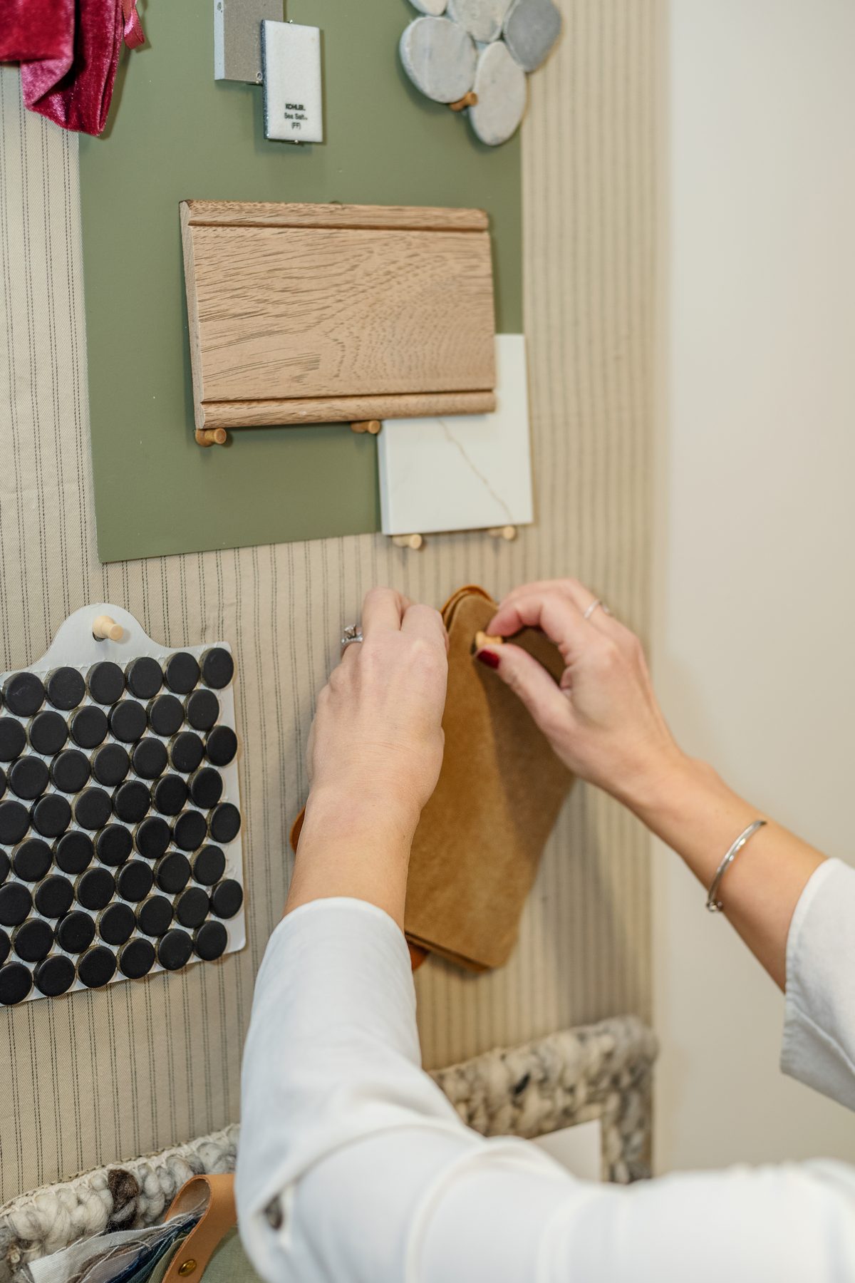 Hands pinning a tan leather swatch to a mood board of wood, tile and stone samples.