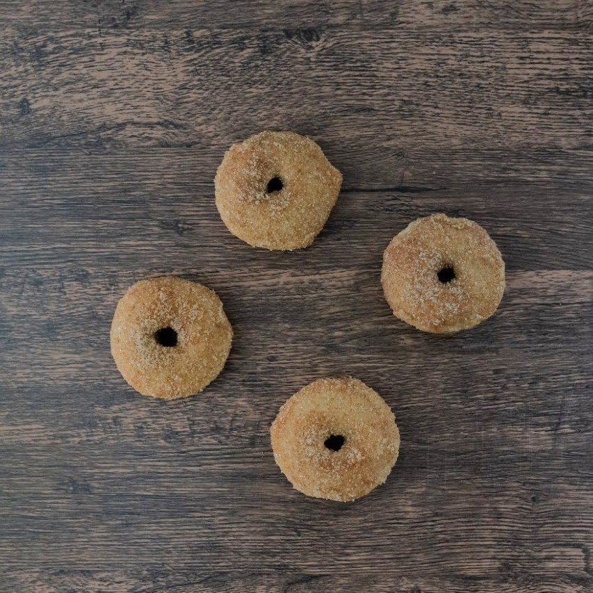 First frame of a stop-motion sequence: four cinnamon-sugar donuts scattered across a dark wood surface.