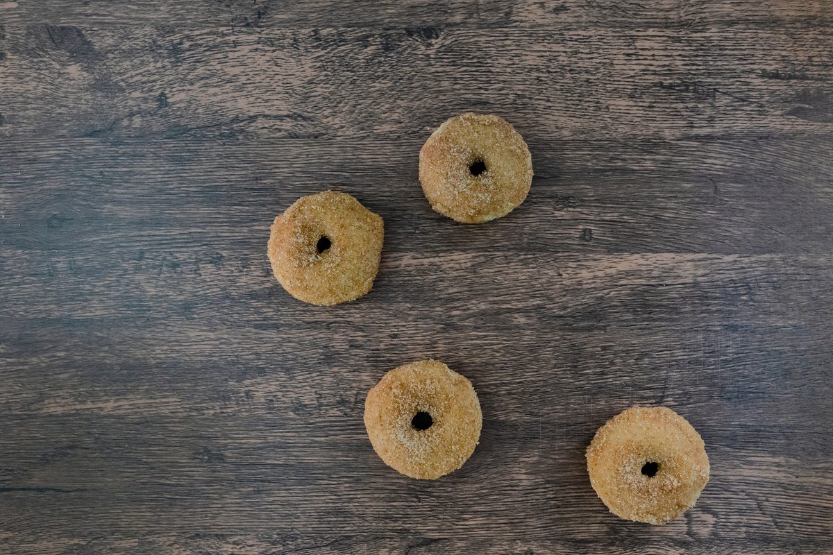 Four small sugared donuts arranged on a weathered dark wood surface, photographed from above.