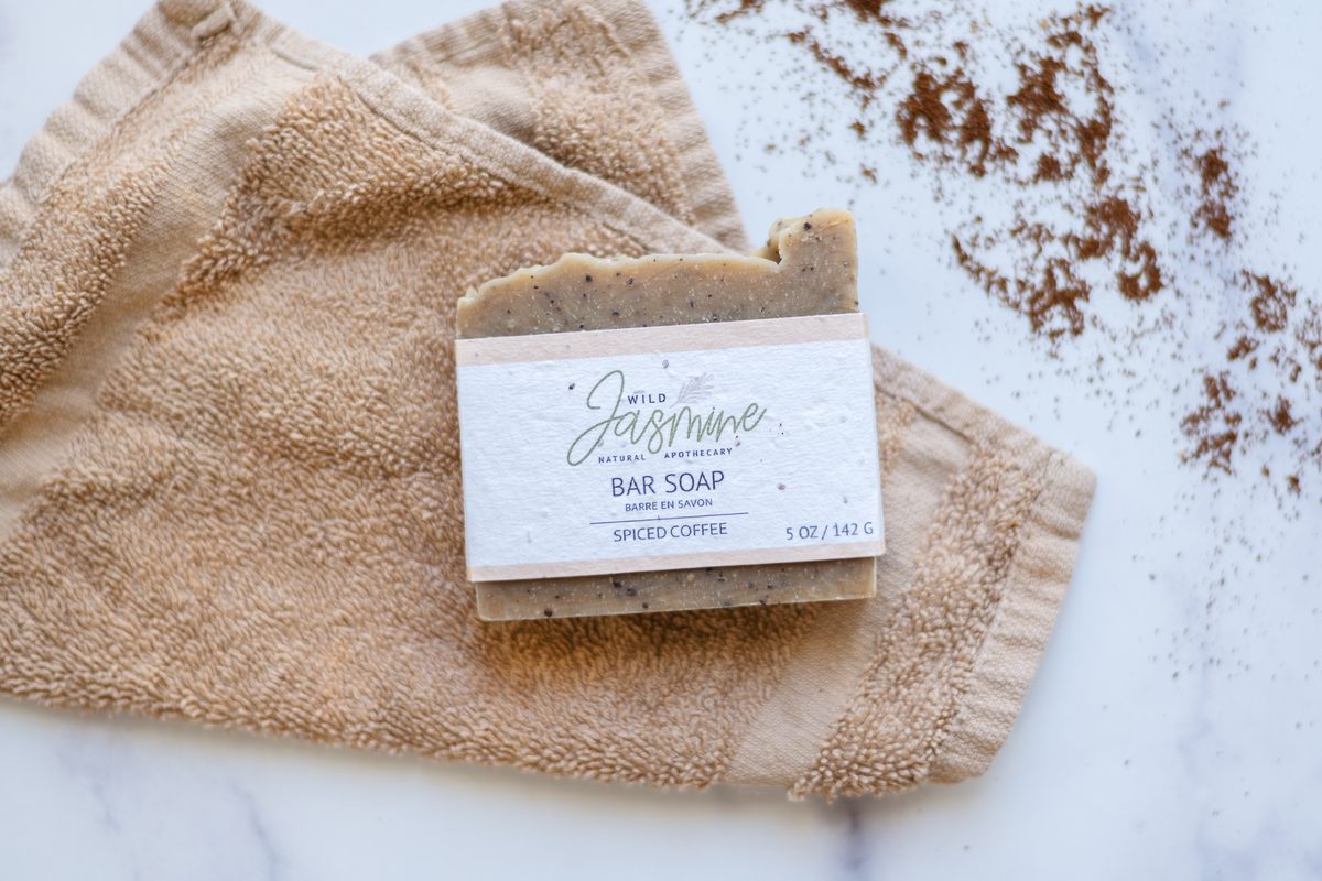 A bar of Wild Jasmine soap resting on a tan washcloth over white marble, with ground spice scattered across the surface.