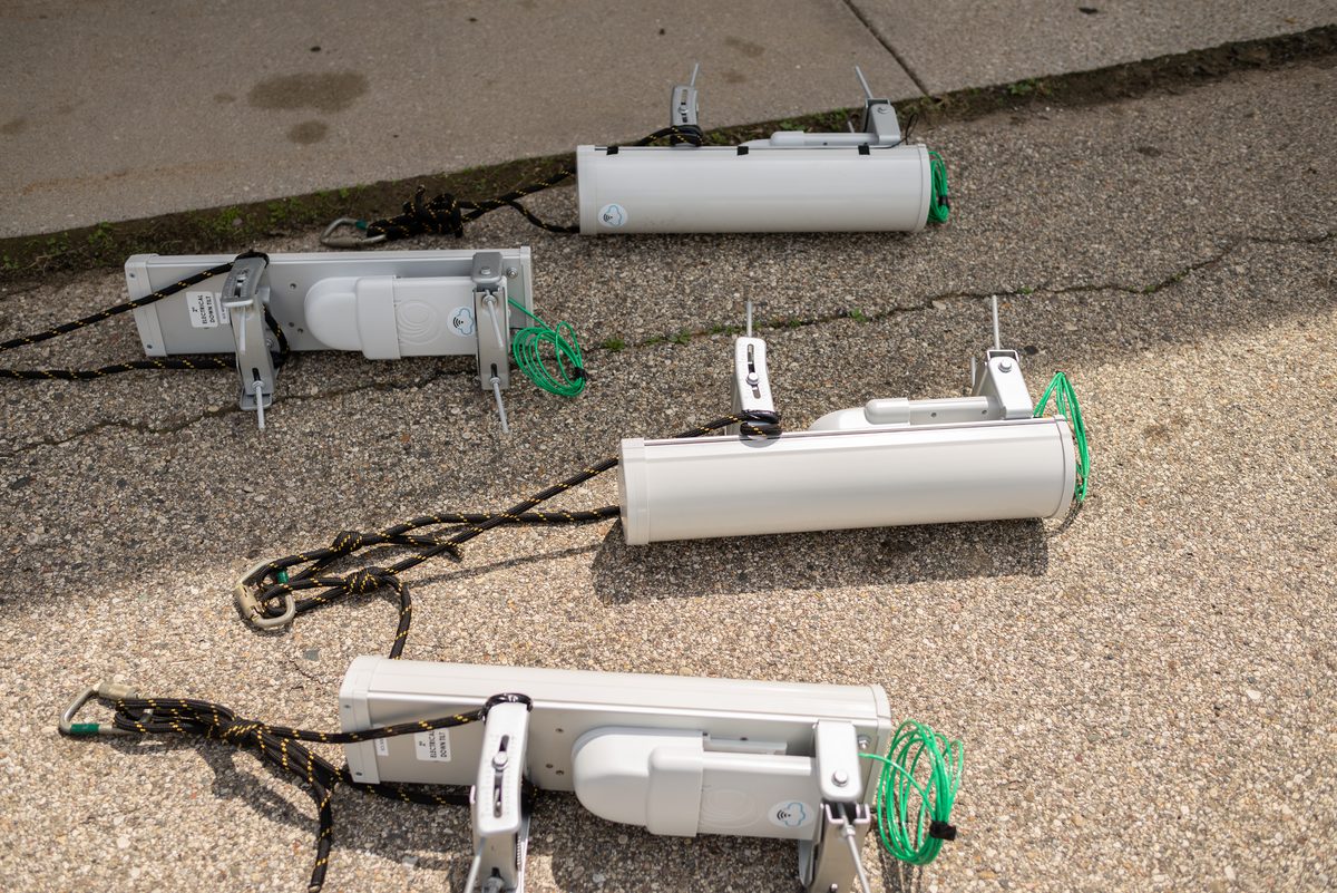 Three white outdoor lighting fixtures with green cables laid out on cracked asphalt.